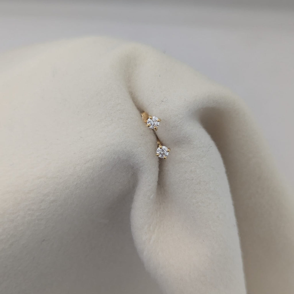 Gold earring with clear gemstones on a person's ear against a neutral background