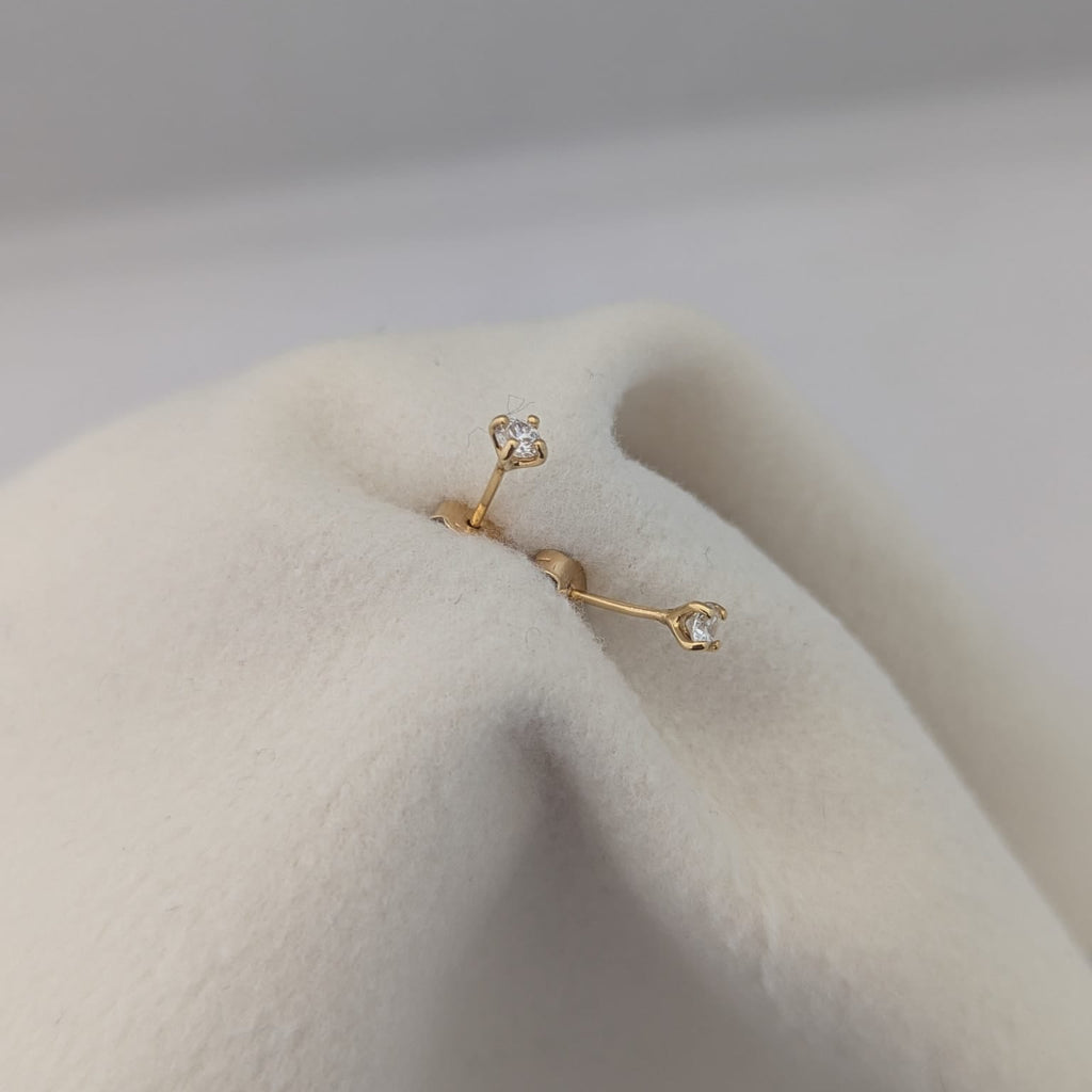 Gold earring on a white cushion with a light gray background
